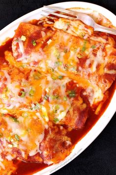 a white plate topped with lasagna covered in cheese and green onions next to a fork