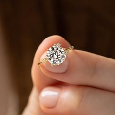 a woman's hand holding a ring with a diamond on it and the middle finger