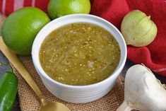 a white bowl filled with green liquid next to limes and garlic on a table