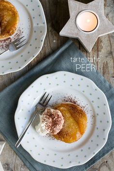 two white plates topped with pastries on top of a wooden table next to a candle