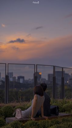 a woman sitting on top of a wooden bench next to a lush green field under a cloudy sky