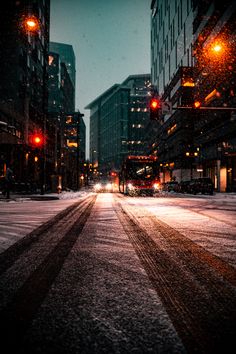 an empty city street at night with snow on the ground and buildings in the background