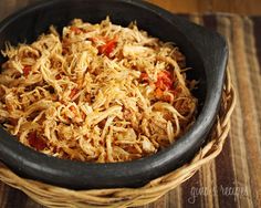 a black bowl filled with shredded food on top of a wooden table next to a basket