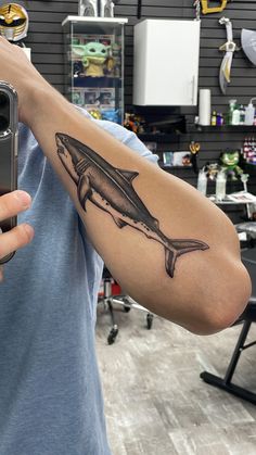 a man with a shark tattoo on his arm taking a selfie in the mirror