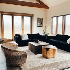 a living room with black couches and wooden tables in front of large glass windows