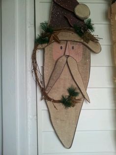 a door hanger with a wooden face wearing a hat and green garland on it