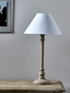 a white lamp sitting on top of a wooden table next to a framed photo and painting