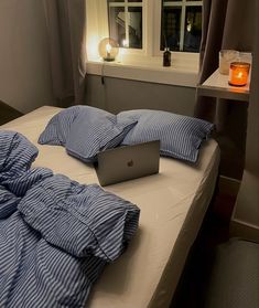 a laptop computer sitting on top of a bed in front of a window next to a lit candle