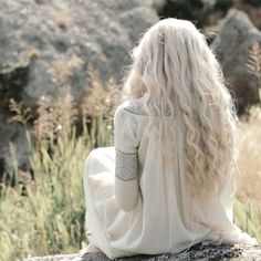 a woman sitting on top of a rock next to tall grass and rocks in the background