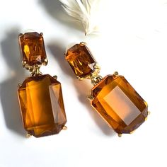 A beautiful pair of early mid century golden topaz faceted glass dangle clip on earrings.  This fabulous pair is designed with simple luxury with 2 rectangle cushion cut glass stones per earring.  The smaller on the top is closed in the back and the larger bottom drop is open backed allowing for maximum light exposure and a divine golden glow.  The earrings measure 1 5/8 inches long with a 1 1/16 inch drop X 1 3/4 inches wide (at the widest part).   These earrings are in excellent condition All Rectangle Cushion, Simple Luxury, Golden Glow, Faceted Glass, Cushion Cut, Cut Glass, Vintage Earrings, Clip On, Clip On Earrings