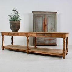 an old wooden table with a potted plant on top and a cabinet behind it