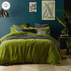 a bed with green sheets and pillows in a blue room next to potted plants