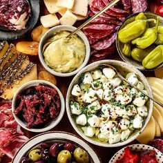 many different types of food in bowls on a wooden table with cheese, olives and pickles