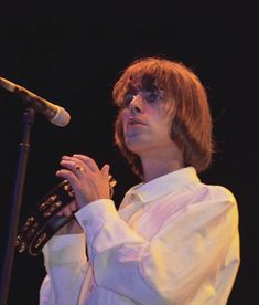 a woman standing in front of a microphone and holding her hands to her chest while wearing glasses