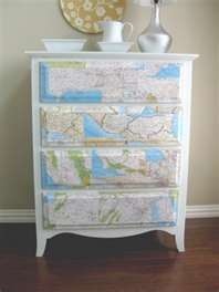 a white dresser with maps on it and a vase sitting on top of the dresser