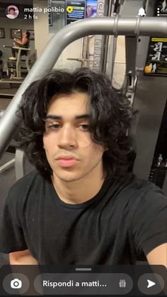 a man with long black hair sitting in a gym looking at the camera and smiling