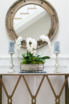 a vase with white flowers on top of a table in front of a round mirror