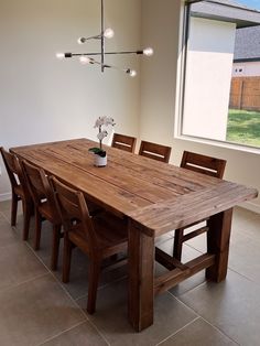 a wooden table and chairs in front of a window with a vase on the table