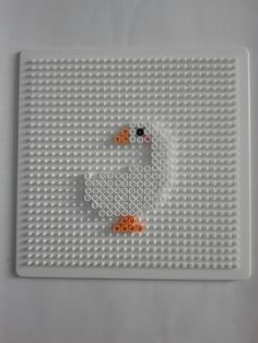 a white lego board with orange and black beads on the bottom, and a smiley face in the middle