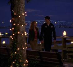 a man and woman standing next to each other in front of a bridge at night