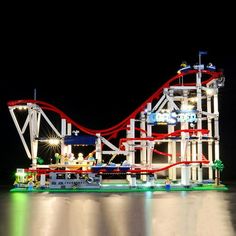 a roller coaster is lit up at night in the water with lights reflecting off it's surface