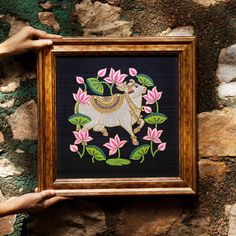 a person holding up a framed art piece with flowers and a dog on it's back