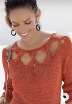 a woman in an orange sweater is looking at her cell phone and smiling while wearing large hoop earrings