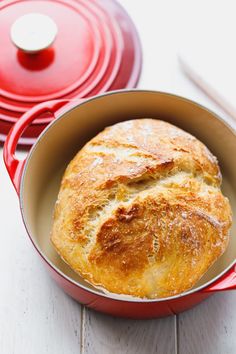 a baked bread in a red pot on a white table next to two red pans