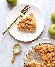 two plates with slices of pie on them next to green apples and a fork,