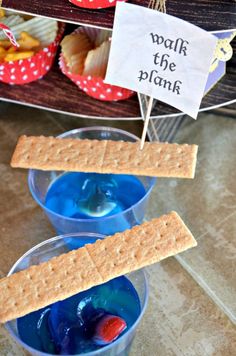 two cups filled with blue liquid and crackers on top of each other next to a sign that says walk the plank