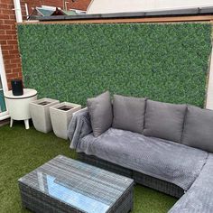 a couch and table on the grass in front of a wall with plants behind it