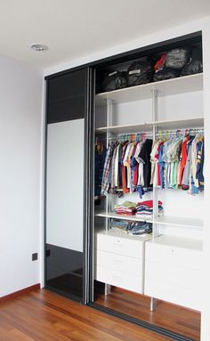 an open closet with clothes and shoes on the shelves next to a wall mounted mirror