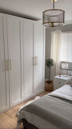 a bedroom with white closets and wood flooring next to a bed in front of a window