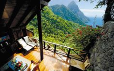 an outdoor deck with chairs and a hot tub overlooking the water, mountains and trees