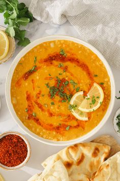 a white bowl filled with soup next to some pita bread and lemon wedges