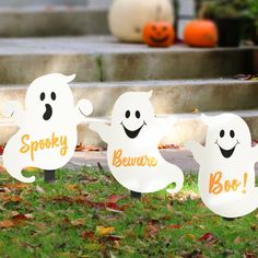 three halloween ghost yard signs sitting in the grass