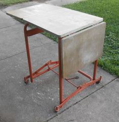 an old school desk sitting on top of a red cart next to a grass field