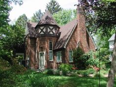 an old brick house in the middle of some trees and grass with bushes around it