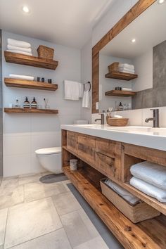 a bathroom with wooden shelving and white towels on the shelves above the sink, along with a toilet