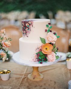 a white wedding cake with flowers on it sitting on a table next to other desserts