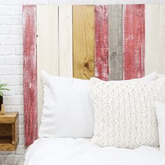 a white bed topped with pillows next to a wooden headboard and night stand in front of a brick wall