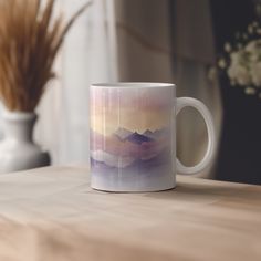 a coffee mug sitting on top of a wooden table next to a vase with flowers