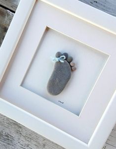 a small rock in a white frame with a blue ribbon hanging from it's side