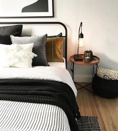 a white bed with black and gold pillows in a bedroom next to a wooden side table