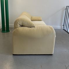 a white couch sitting next to a tall green pole in a room with concrete floors