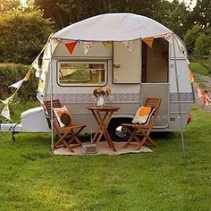 an rv is parked in the grass with two chairs and a table set up next to it