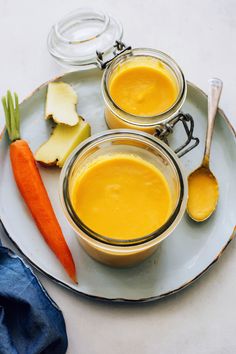 two jars filled with orange liquid sitting on top of a plate next to carrots