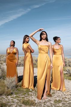 three women in yellow dresses standing on the ground with their hands behind their head and looking up at the sky