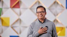 a man standing in front of a colorful wall and holding his hands together while smiling at the camera