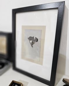 two framed photographs sitting next to each other on a white counter top with black trim around the edges